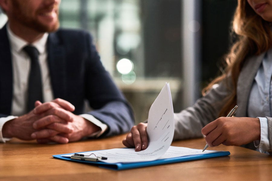 Two people reviewing documents, one signing, in an office setting.