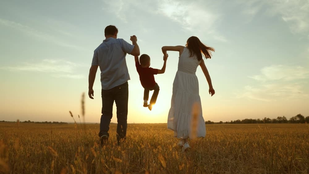 Mom dad kid hold hands at sunset.