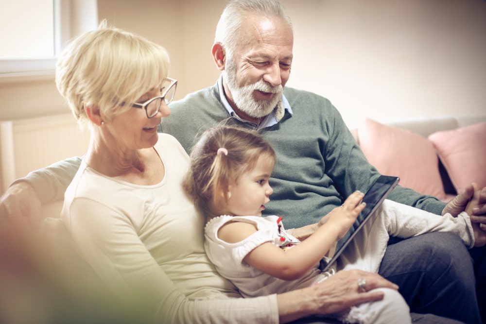 An Elderly Couple And Their Grandchild Playing On A Tablet