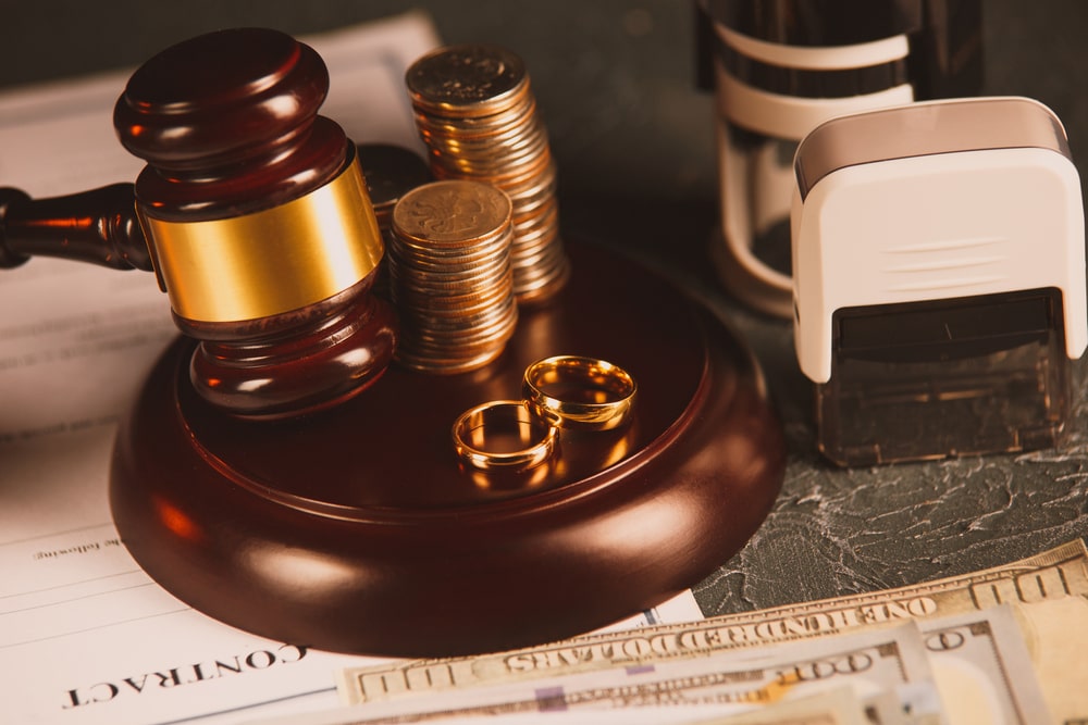 Coins And A Pair Of Golden Rings Set Behind A Judges Hammer