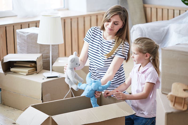 A Mom And Her Daughter Unpacking Toys From Cardboard Boxes