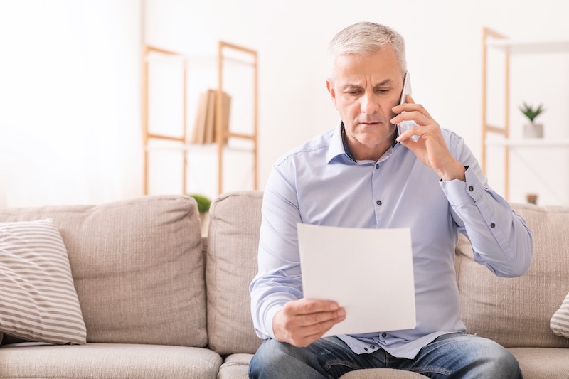 Legal Questions Man Sitting On A Couch Talking On The Phone And Reading A Document