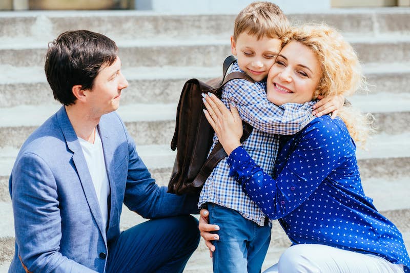Smiling Child A Child Hugging A Woman Next To Another Man