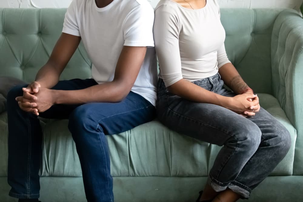 Unhappy married couple sit on couch turn back not talking ignore each other