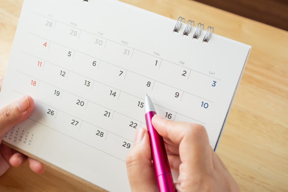 Calendar page with female hand holding pen on desk table