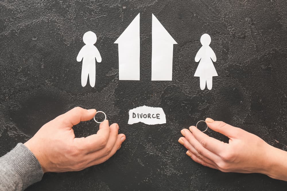 Male and female hands with wedding rings, cut figures of house and couple on dark background
